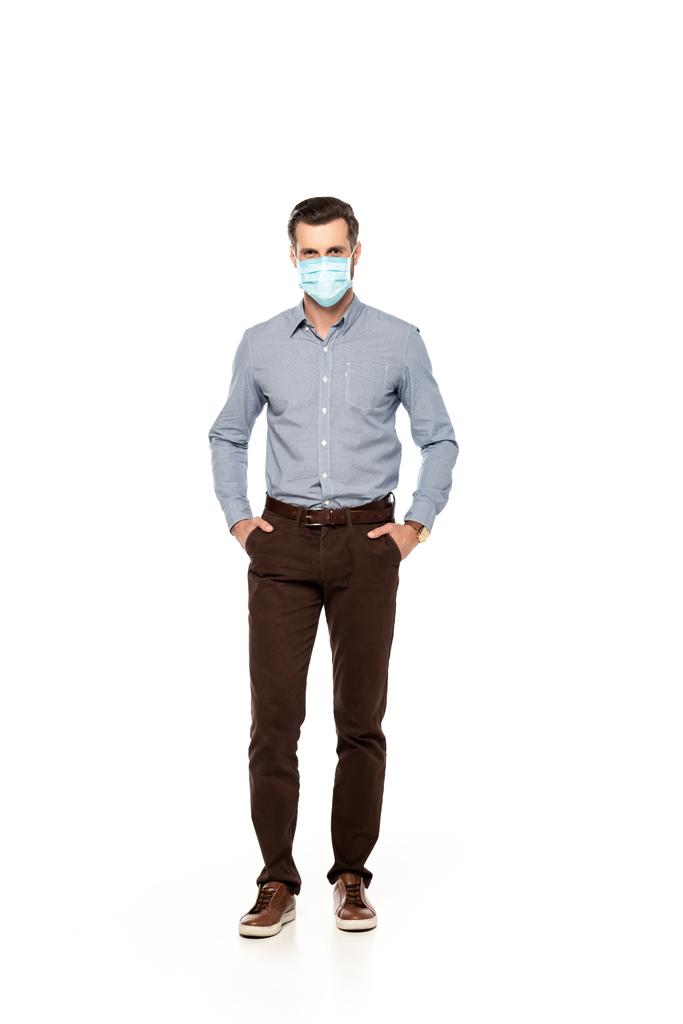hombre de negocios en máscara médica de pie con las manos en bolsillos aislados en blanco
  - Foto, imagen