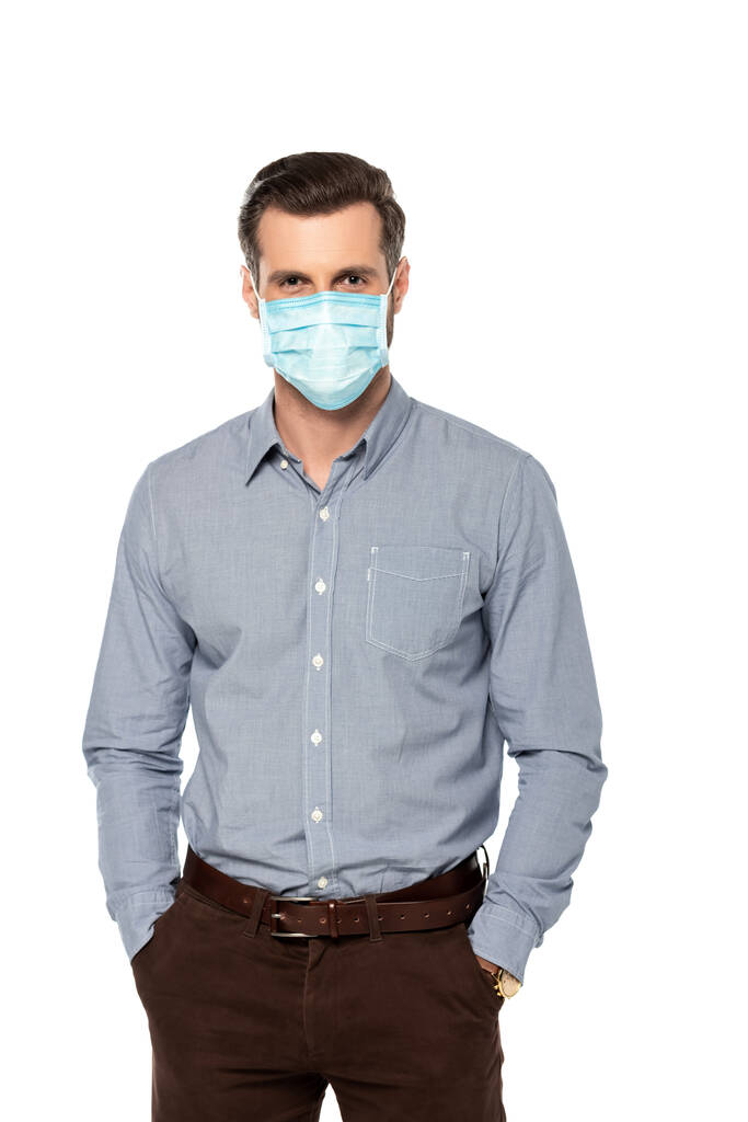 uomo d'affari in maschera medica blu in piedi con le mani in tasche isolate su bianco
  - Foto, immagini
