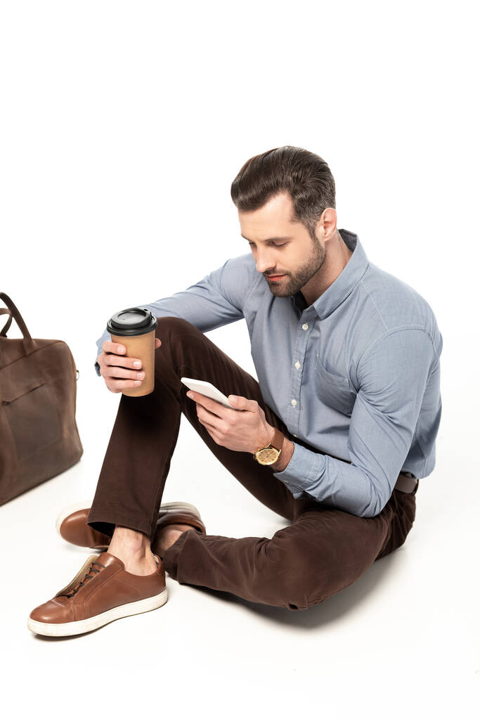 白い袋の近くに座っている間にスマートフォンを使って髭を生やしたビジネスマン  - 写真・画像