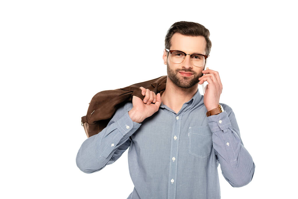 šťastný a vousatý podnikatel drží tašku a mluví na smartphone izolované na bílém   - Fotografie, Obrázek