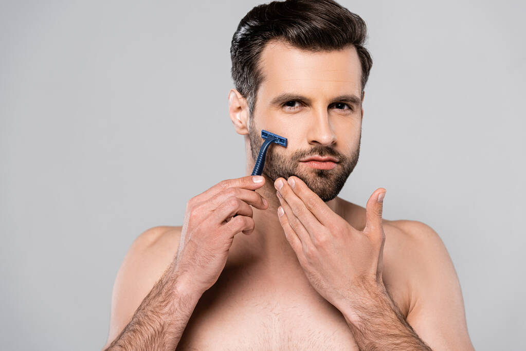 jóképű férfi kezében borotva, miközben borotválkozás elszigetelt szürke  - Fotó, kép