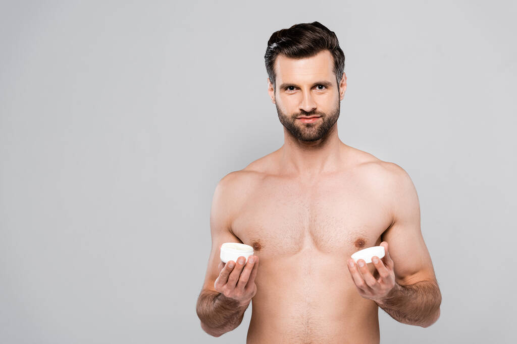 мускулистый человек держит контейнер с косметическим кремом, изолированным на сером
  - Фото, изображение