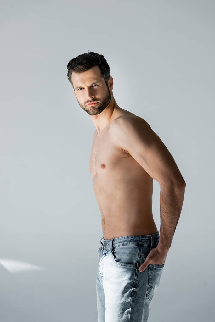 muscular and shirtless man standing with hand in pocket on grey - Photo, Image