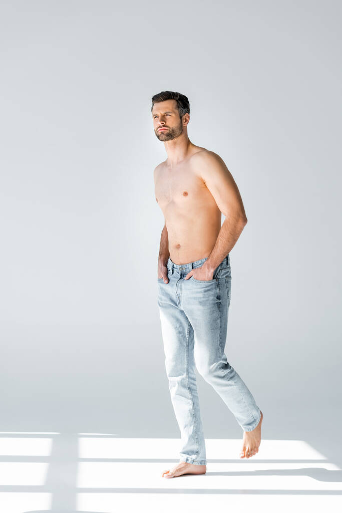 sole su uomo senza camicia in blue jeans che cammina con le mani in tasca su grigio
  - Foto, immagini