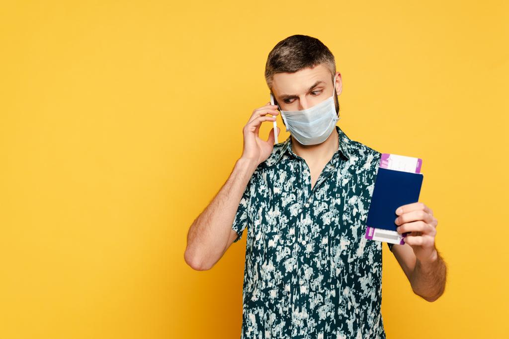 man met medisch masker met paspoort praten op smartphone op geel - Foto, afbeelding