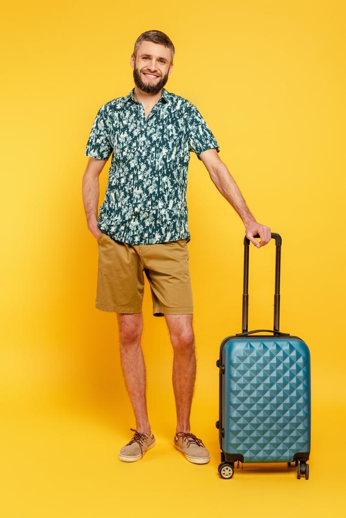 full length view of happy bearded guy with travel bag on yellow - Photo, Image