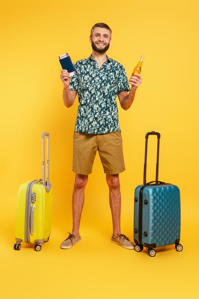 vue pleine longueur du gars barbu heureux avec des sacs de voyage, bière et passeport sur jaune
 - Photo, image