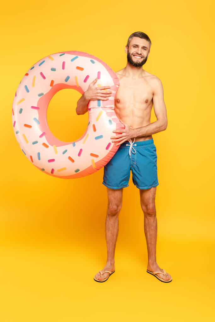 Ganzkörperansicht des glücklichen bärtigen Kerls mit Schwimmring auf gelb - Foto, Bild