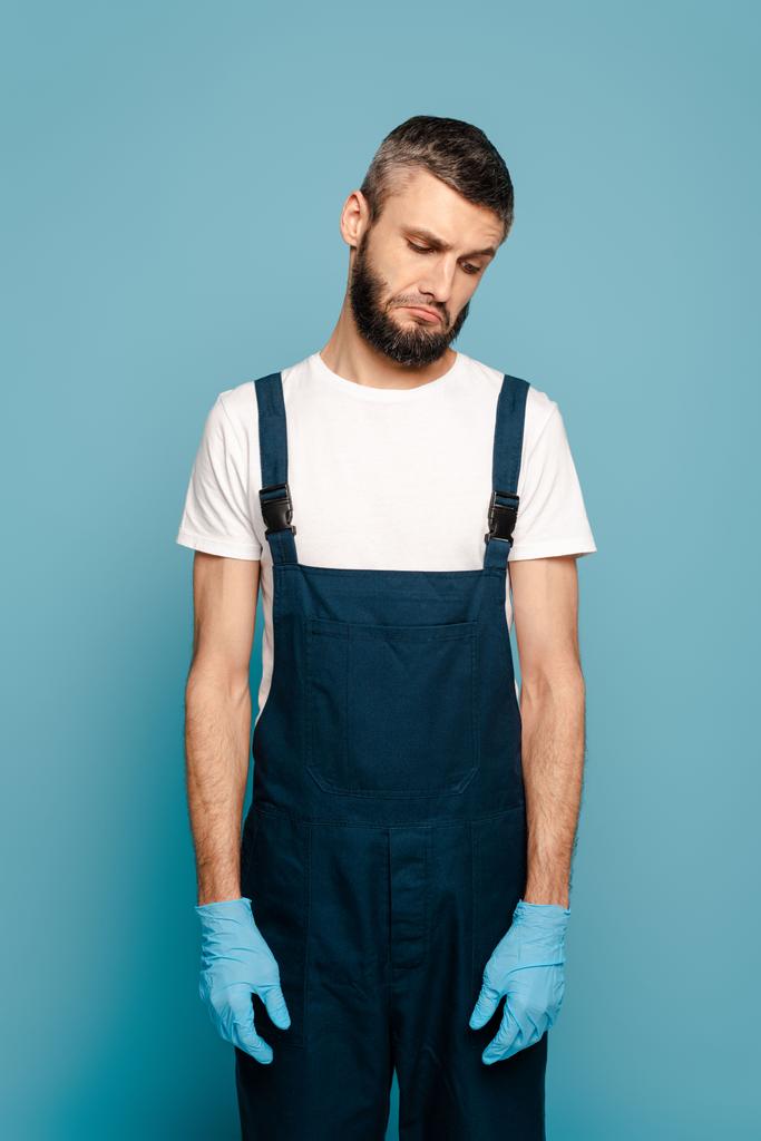 limpiador triste en uniforme y guantes de goma sobre fondo azul
 - Foto, Imagen