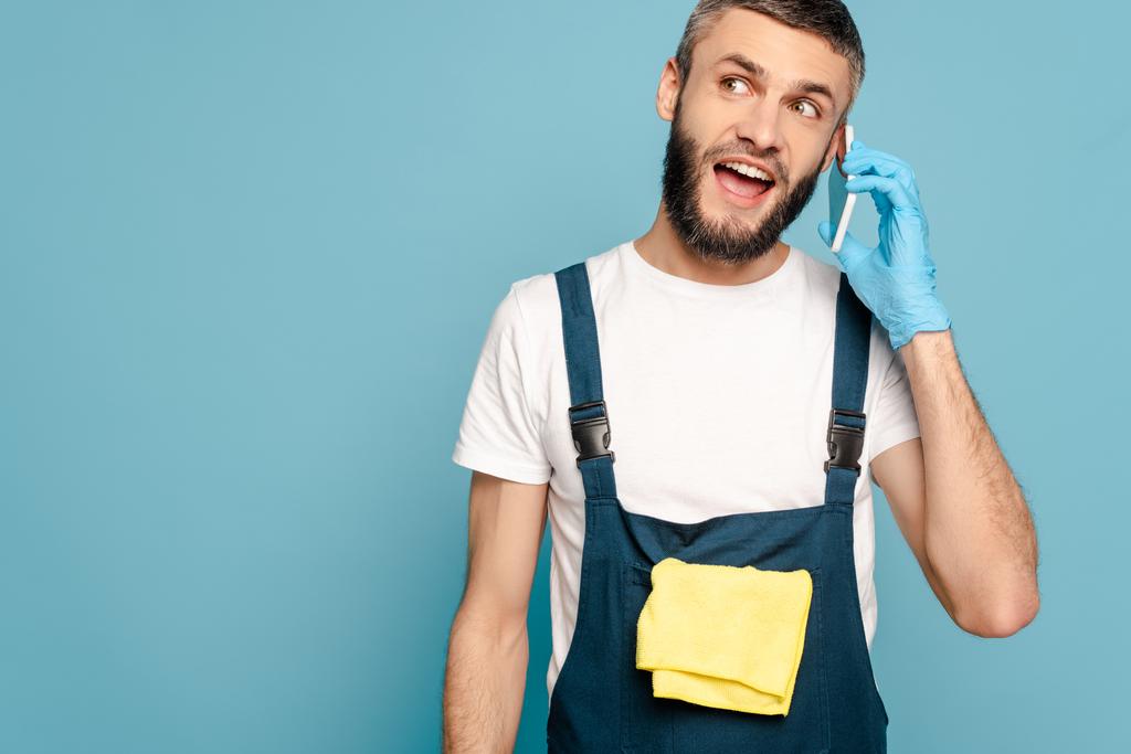 detergente eccitato in uniforme e guanti di gomma con tappeto parlare su smartphone isolato su blu
 - Foto, immagini