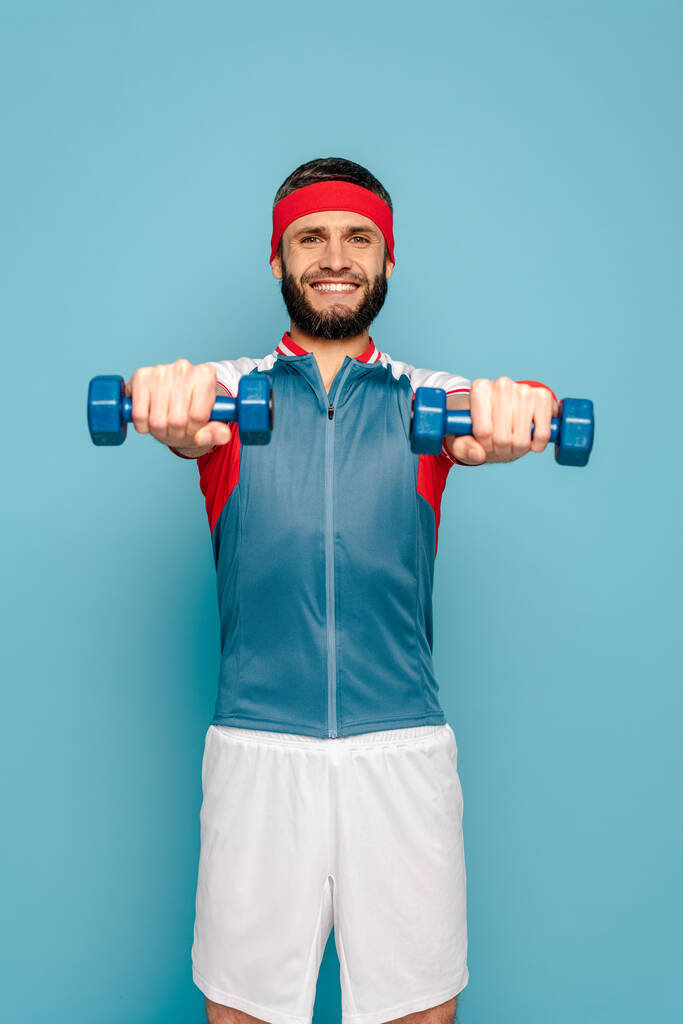 mosolygós stílusos sportoló gyakorló súlyzók kék háttér - Fotó, kép