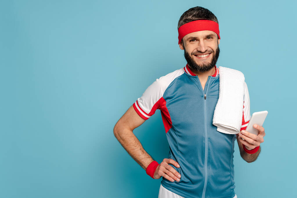 усміхнений стильний спортсмен з рушником за допомогою смартфона на синьому фоні
 - Фото, зображення