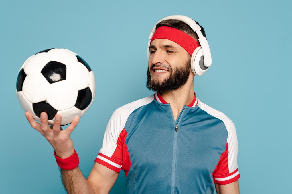 happy stylish sportsman in headphones with soccer ball on blue background - Photo, Image
