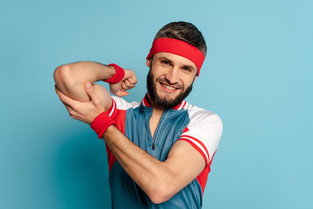 sonriente deportista con estilo tocando bíceps sobre fondo azul
 - Foto, imagen