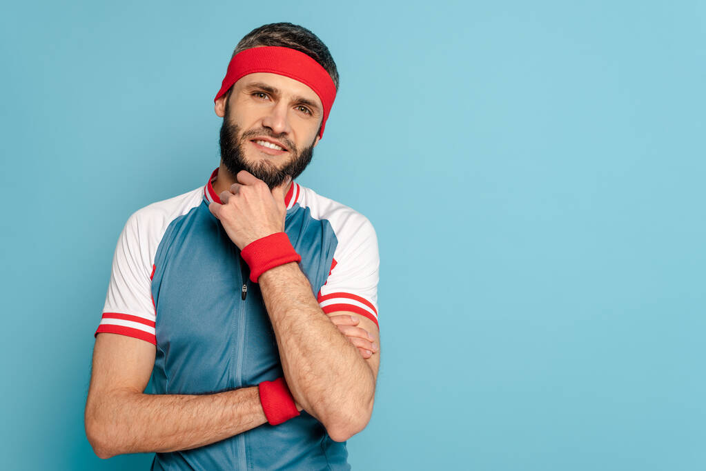 sonriente deportista con estilo tocando la barbilla sobre fondo azul
 - Foto, imagen