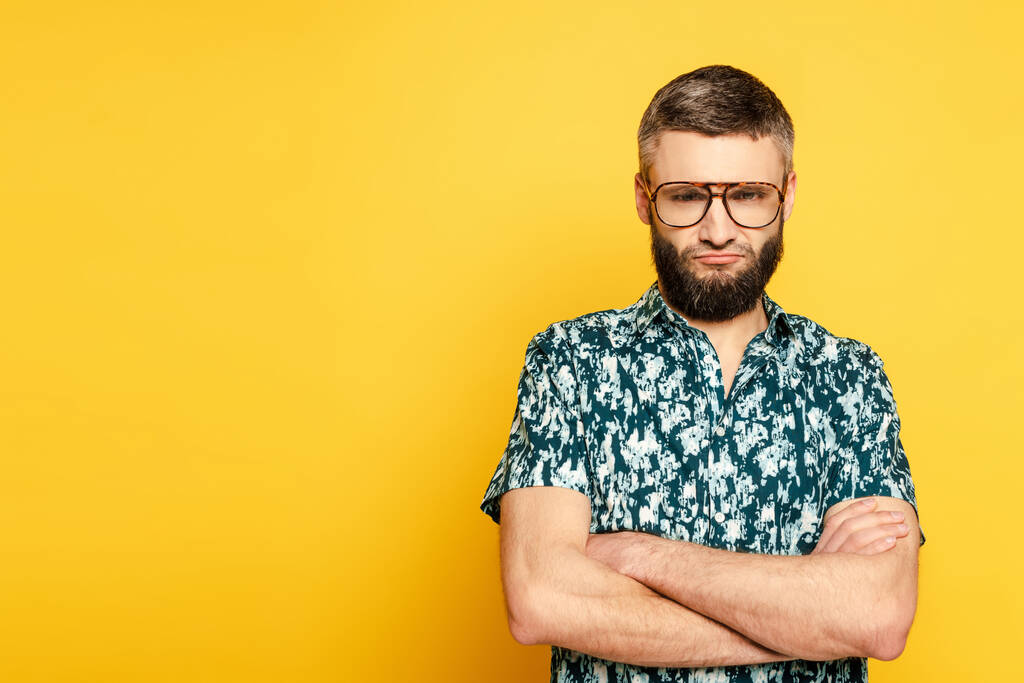 обиженный бородатый парень в очках со скрещенными руками на желтом
 - Фото, изображение