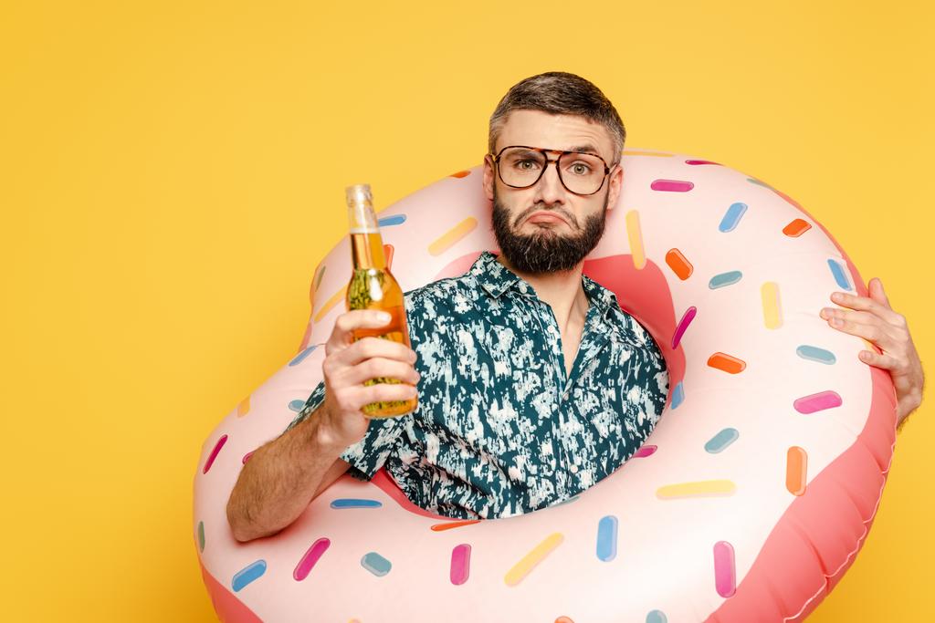 triste barbu gars dans des lunettes et anneau de natation avec bouteille de bière sur jaune
 - Photo, image