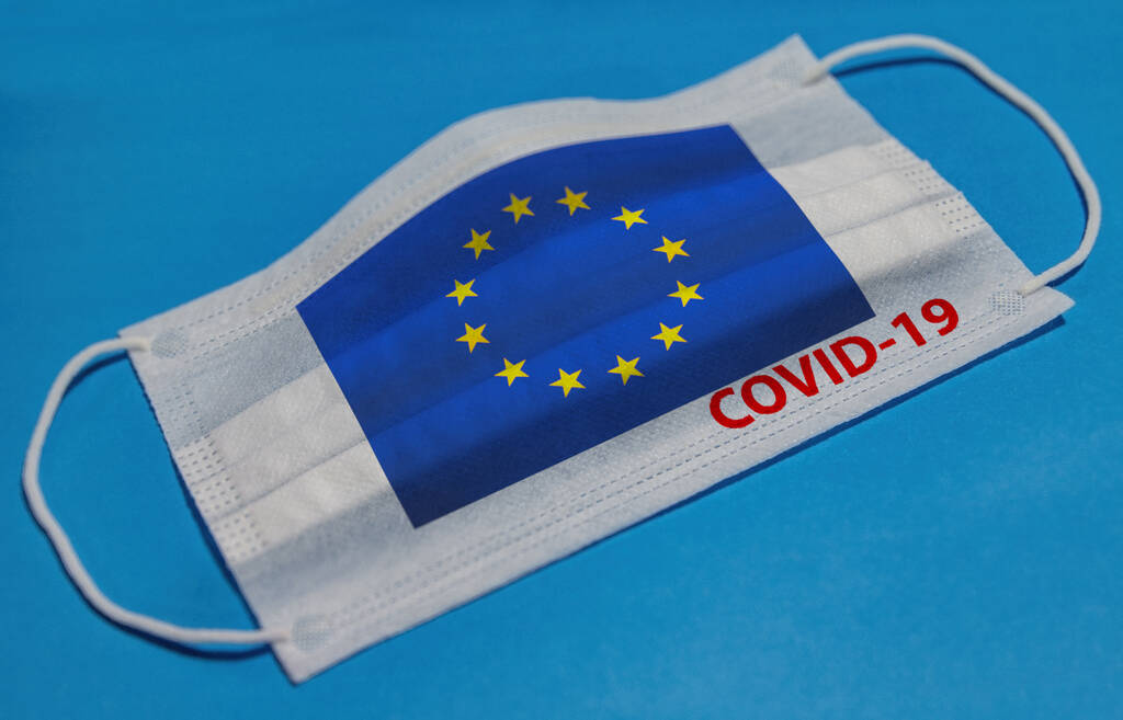 Máscara facial médica con bandera de la Unión Europea y texto COVID-19 sobre fondo azul. Concepto de cuarentena por coronavirus
. - Foto, imagen