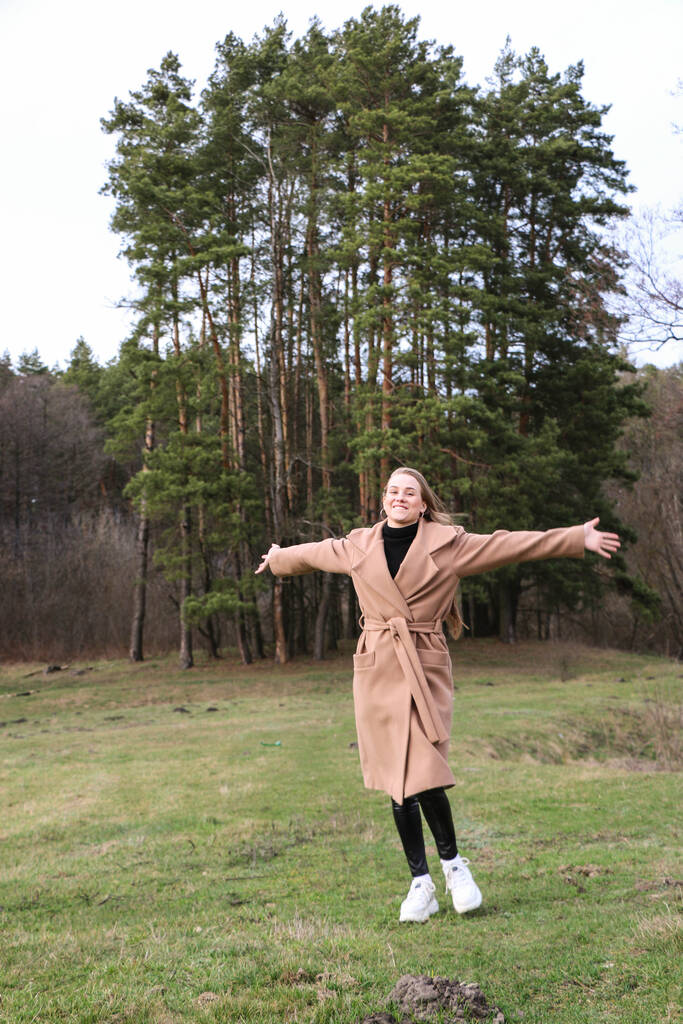 hermosa chica, rubia con el pelo largo, camina en la primavera cerca del bosque en un abrigo marrón., serenidad y libertad
 - Foto, imagen