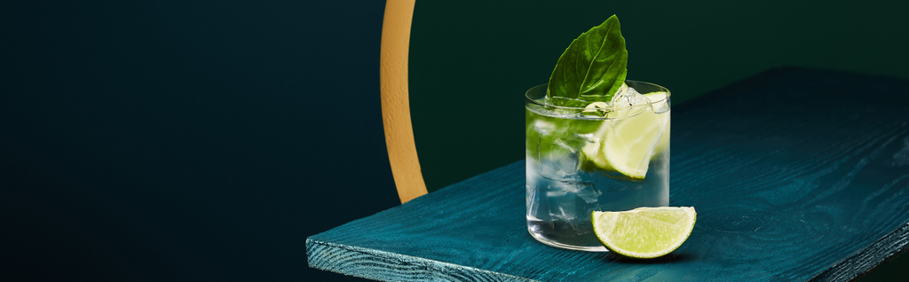 Vidro com bebida refrescante com fatia de limão, gelo e folha de hortelã na superfície de madeira em fundo geométrico azul e verde
 - Foto, Imagem