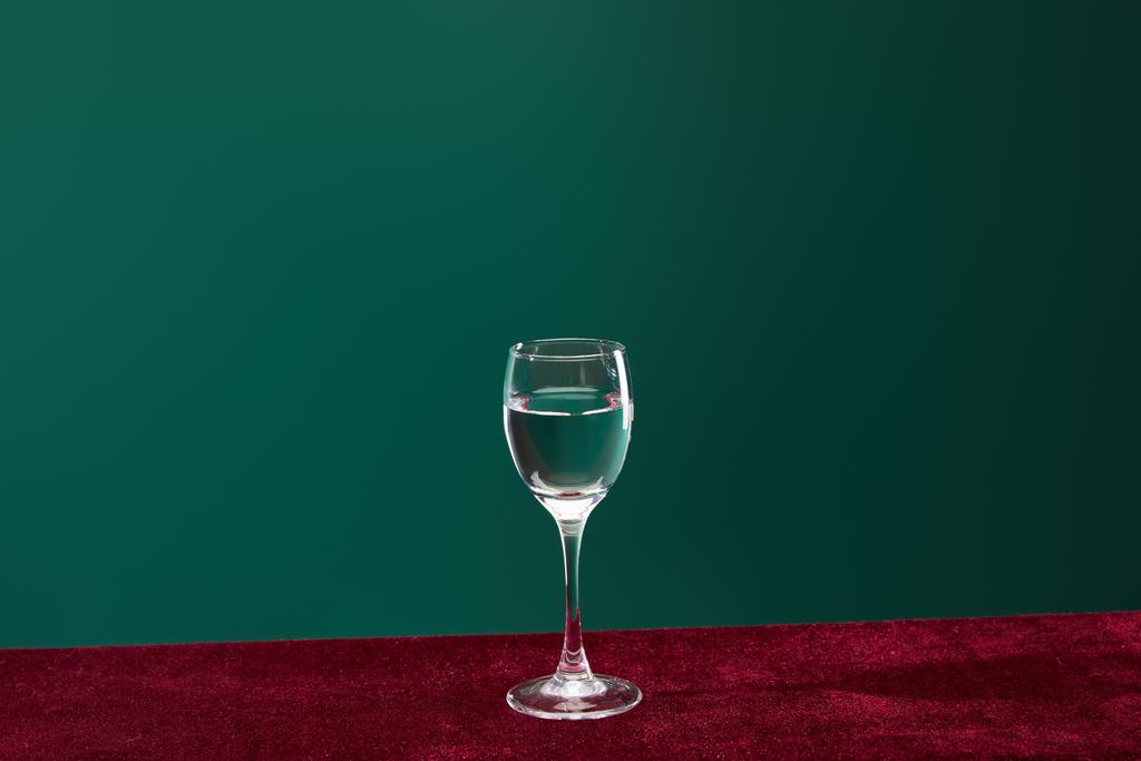 σφηνάκι γυάλινο με καθαρό διαφανές υγρό που απομονώνεται σε πράσινο  - Φωτογραφία, εικόνα