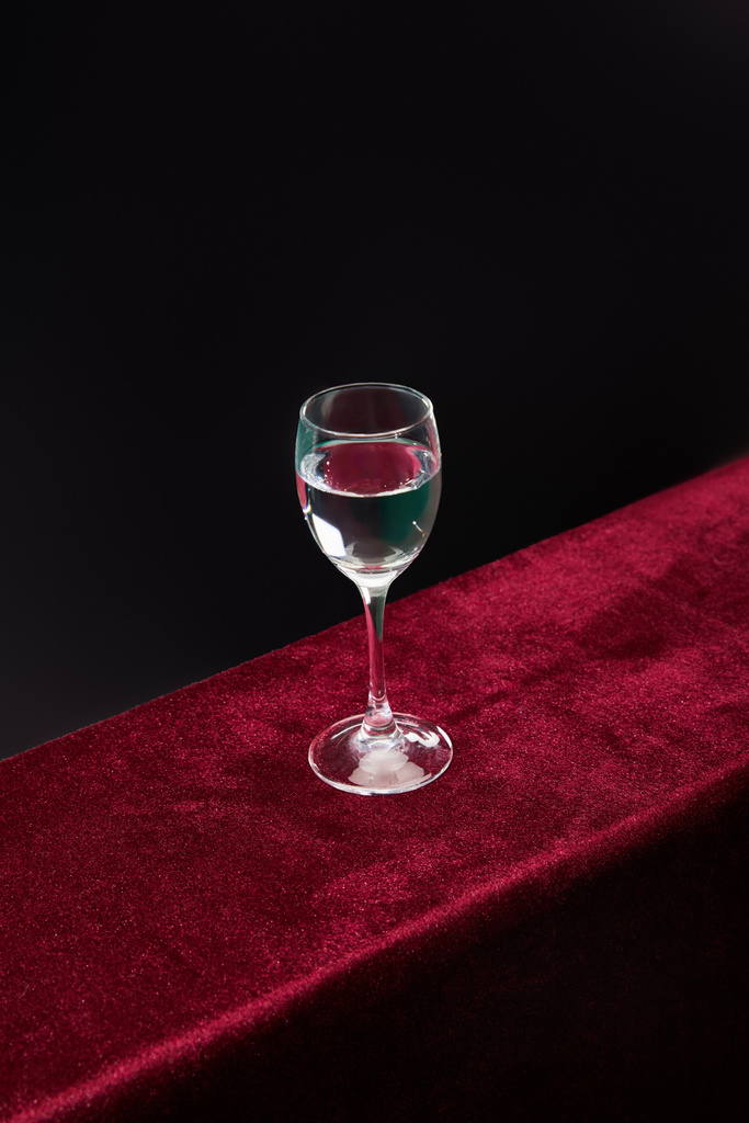 Hoge hoek weergave van shot glas met zuivere transparante vloeistof geïsoleerd op zwart - Foto, afbeelding