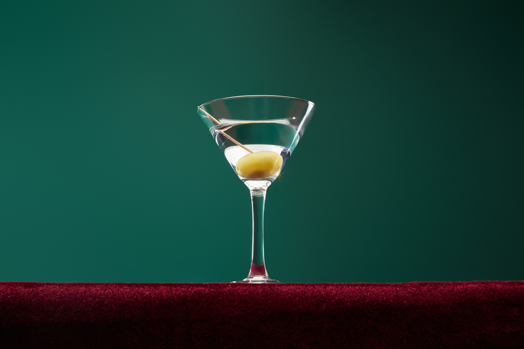 Low angle view of cocktail glass with vermouth and whole olive on toothpick isolated on green - Photo, Image