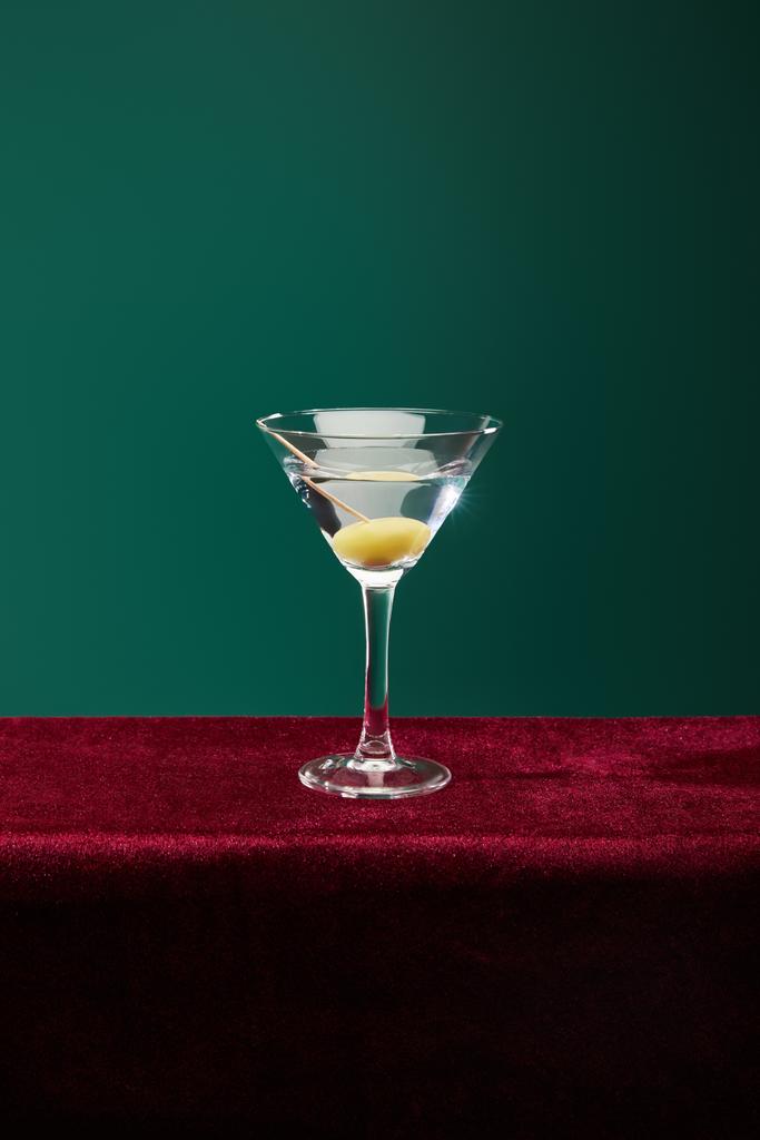 Vermutlu kristal kokteyl bardağı ve yeşilde izole edilmiş kürdanlı zeytin. - Fotoğraf, Görsel
