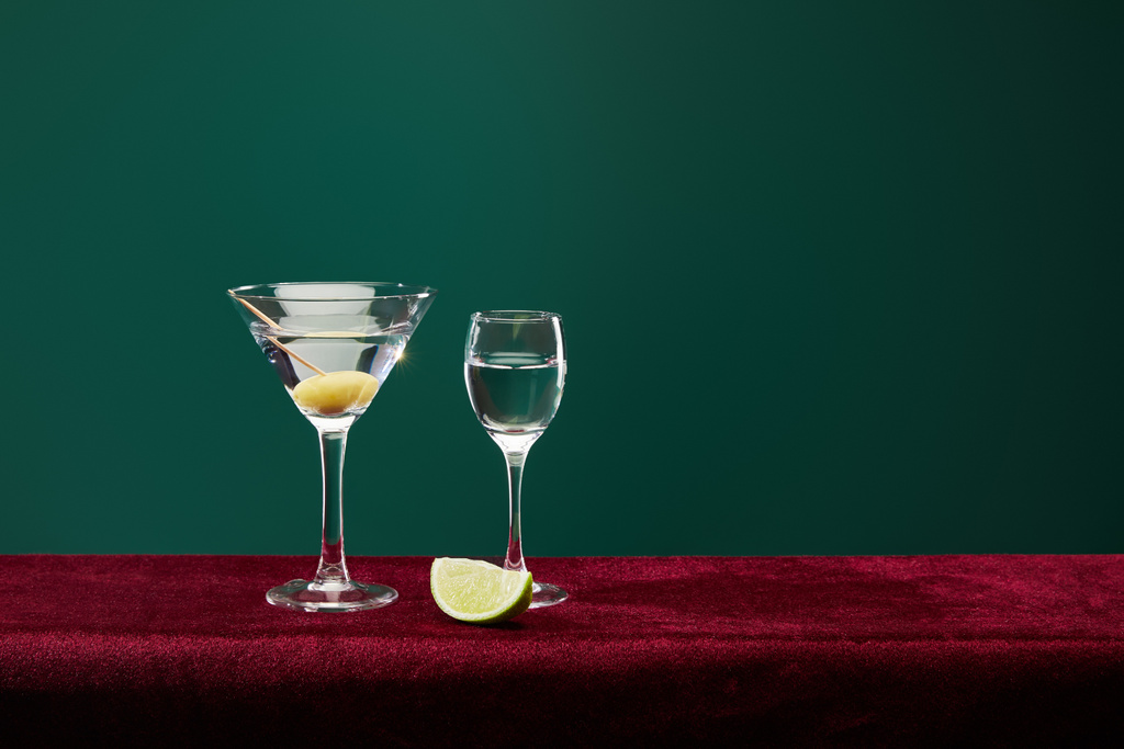 shot glass and cocktail glass with vermouth, lime slice and whole olive on toothpick on velour surface isolated on green   - Photo, Image
