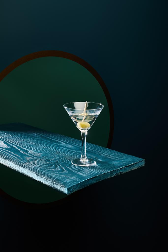 copo de coquetel com vermute e azeitona inteira no palito na superfície de madeira azul no fundo geométrico
 - Foto, Imagem