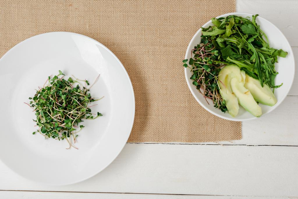 vista superior de microgreen fresco en el plato cerca de tazón de ensalada verde en servilleta beige en la superficie de madera blanca
 - Foto, Imagen