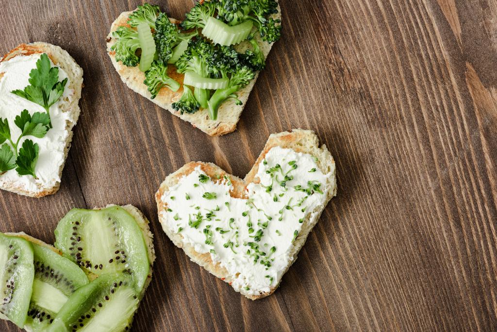 Kalbin üst görüntüsü krem peynir, brokoli, mikroyeşil, maydanoz ve kivi ile ahşap yüzey - Fotoğraf, Görsel
