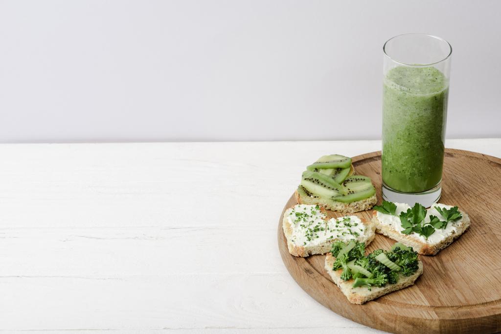 yeşil smoothie ve kalp şeklinde kanape krem peyniri, brokoli, mikroyeşil, maydanoz ve kivi beyaz ahşap yüzeyde - Fotoğraf, Görsel
