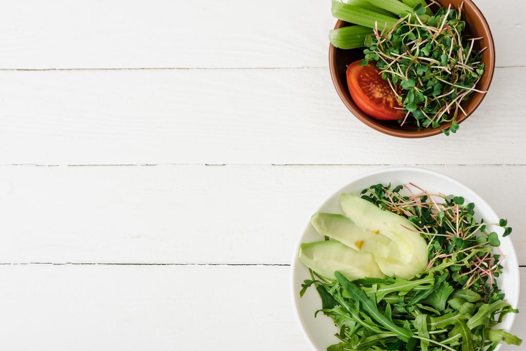 Draufsicht auf frisches Gemüse mit Avocado und Microgreen in Schalen auf weißer Holzoberfläche - Foto, Bild
