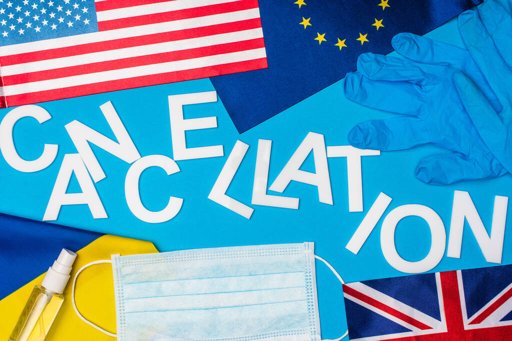 Vista superior do cancelamento de letras perto de máscara médica, luvas de látex e bandeiras de países na superfície azul
 - Foto, Imagem