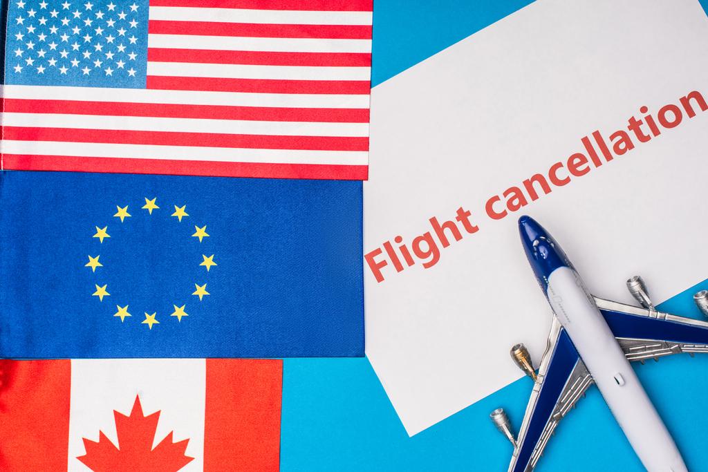 Kanada, Avrupa Birliği ve Amerika 'nın oyuncak uçak yakınlarındaki bayraklarının en üst görüntüsü mavi yüzey üzerindeki uçuş iptal mektuplarıyla - Fotoğraf, Görsel