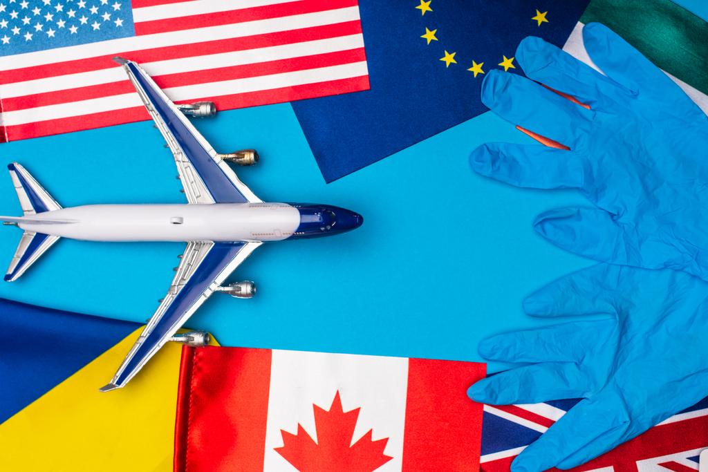 Bovenaanzicht van vlaggen van landen met latex handschoenen en speelgoed vliegtuig op blauwe achtergrond - Foto, afbeelding