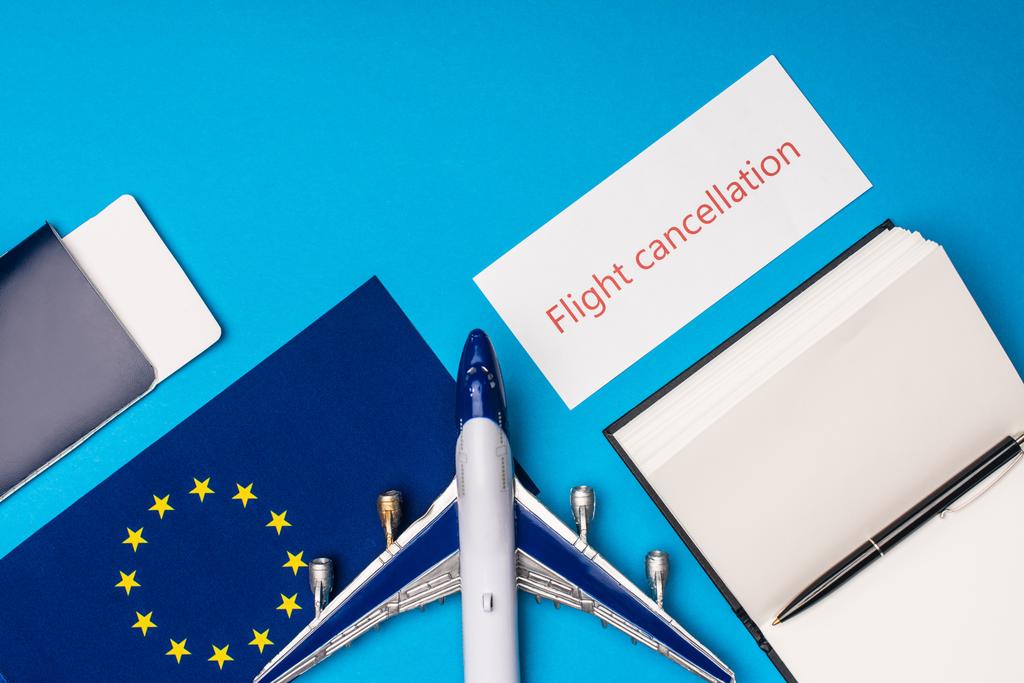 おもちゃの飛行機、パスポート、青い表面にヨーロッパの団結の旗の近くのフライトキャンセルレタリングとカードのトップビュー - 写真・画像