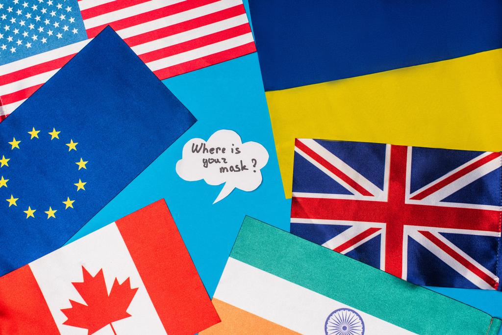 Κορυφή άποψη της φούσκας του λόγου με το πού είναι η μάσκα σας γράμματα κοντά σημαίες των χωρών που απομονώνονται σε μπλε  - Φωτογραφία, εικόνα