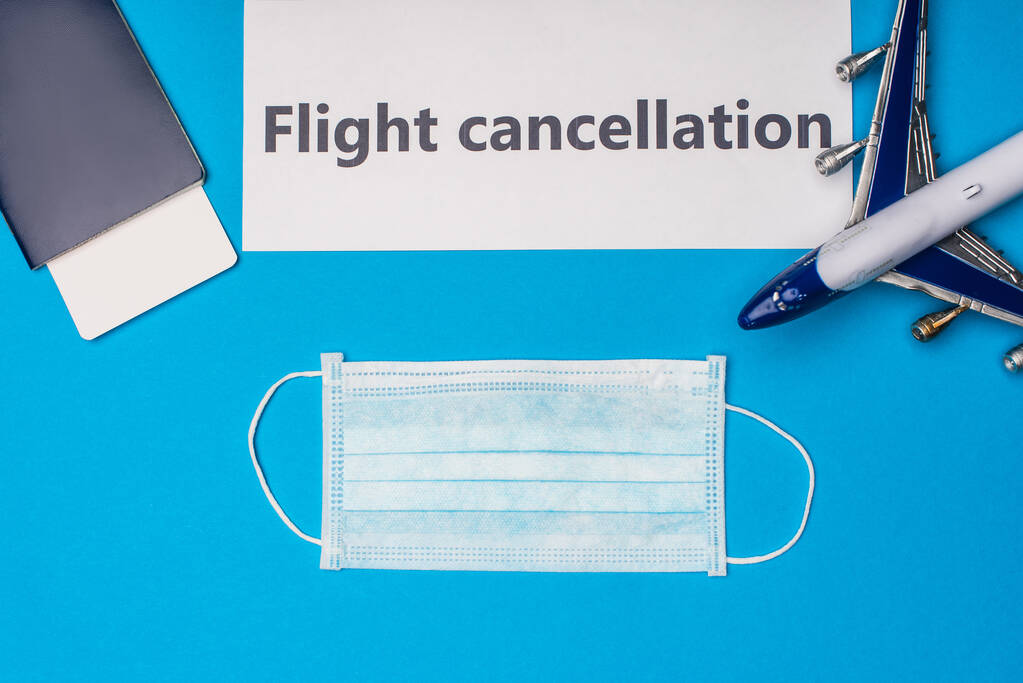 Κάτοψη ιατρικής μάσκας, διαβατηρίου με αεροπορικό εισιτήριο και κάρτας με ακύρωση πτήσης σε μπλε επιφάνεια - Φωτογραφία, εικόνα