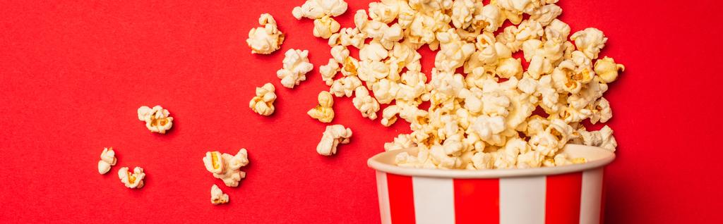 Bovenaanzicht van emmer met popcorn op rode achtergrond, panoramisch schot - Foto, afbeelding
