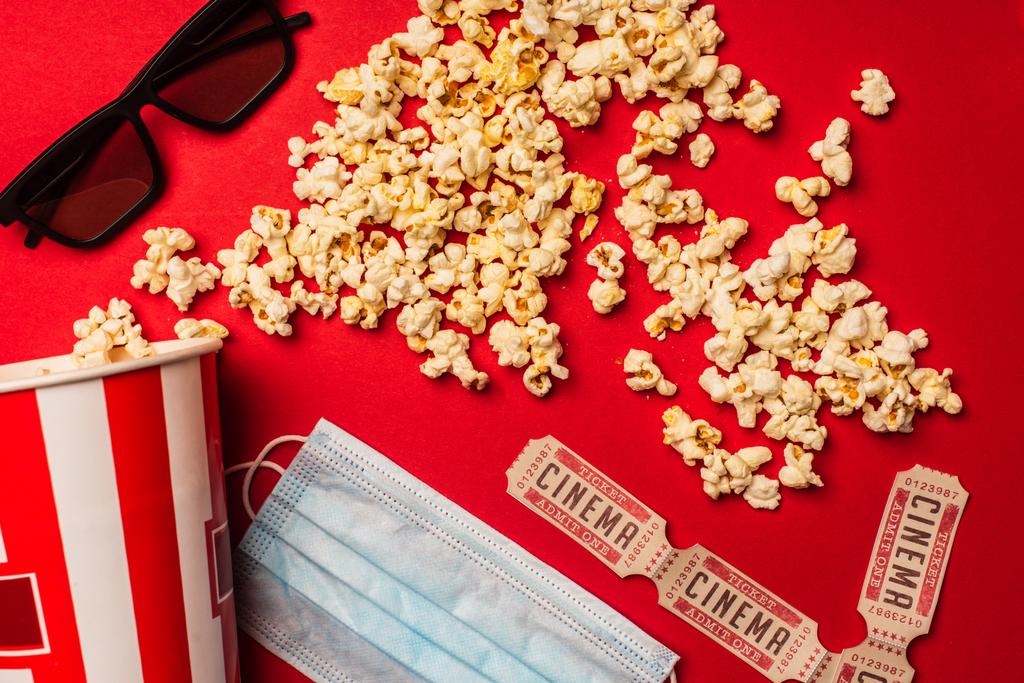 Widok z góry popcorn, maska medyczna z bilety do kina i okulary przeciwsłoneczne na czerwonym tle - Zdjęcie, obraz