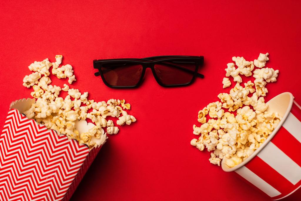 Bovenaanzicht van zonnebril bij emmers met popcorn op rode achtergrond - Foto, afbeelding