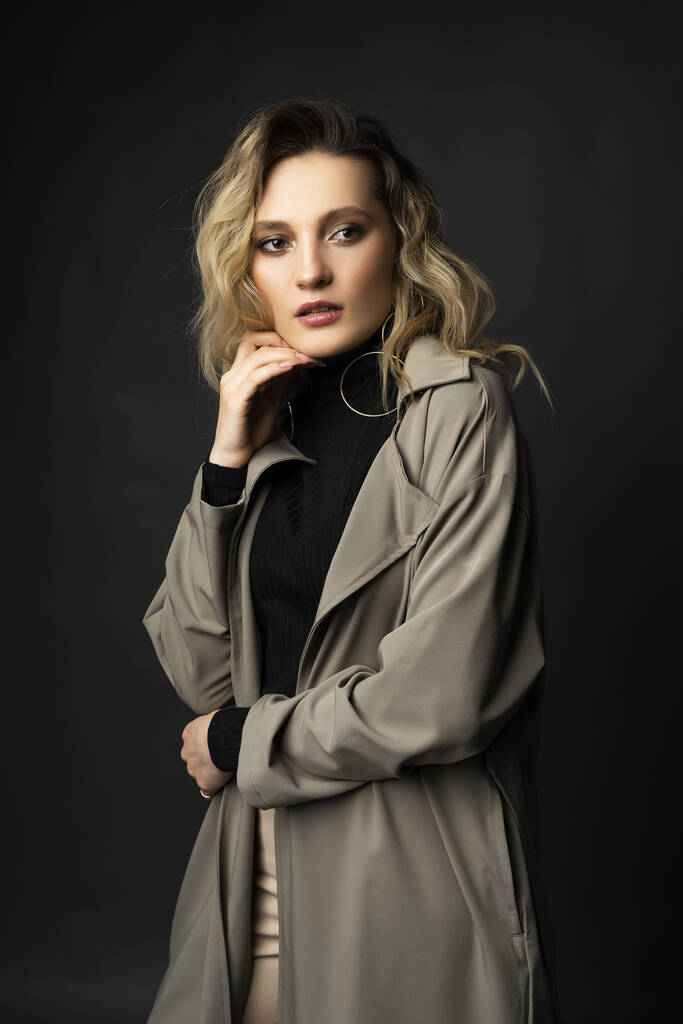 Beautiful girl wearing a casual trendy trousers, turtleneck and raincoat posing on a dark background. Fashionable, advertising, lifestyle and commercial design - Photo, Image