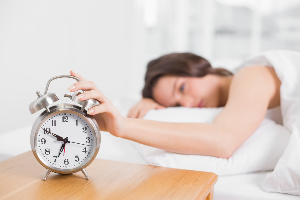 Hämärtynyt nainen sängyssä ulottuu käsi herätyskelloon
 - Valokuva, kuva