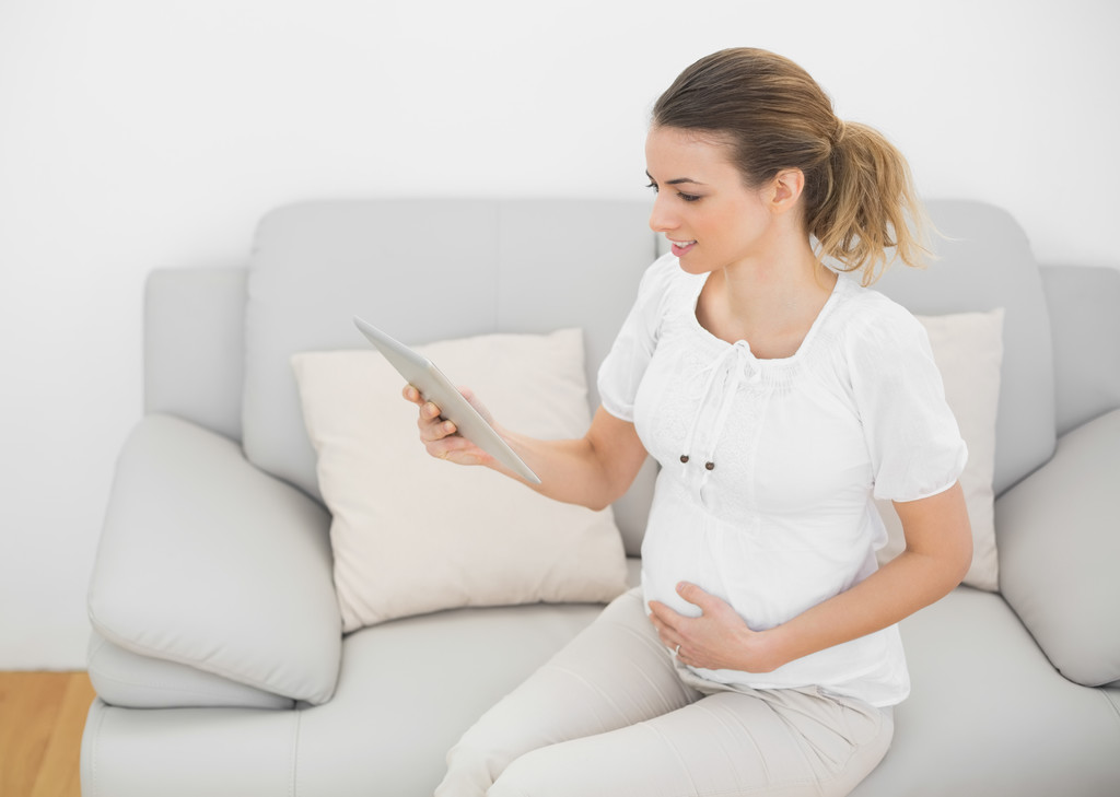 süße schwangere Frau, die ihren Bauch berührt, während sie ihr Tablet benutzt - Foto, Bild
