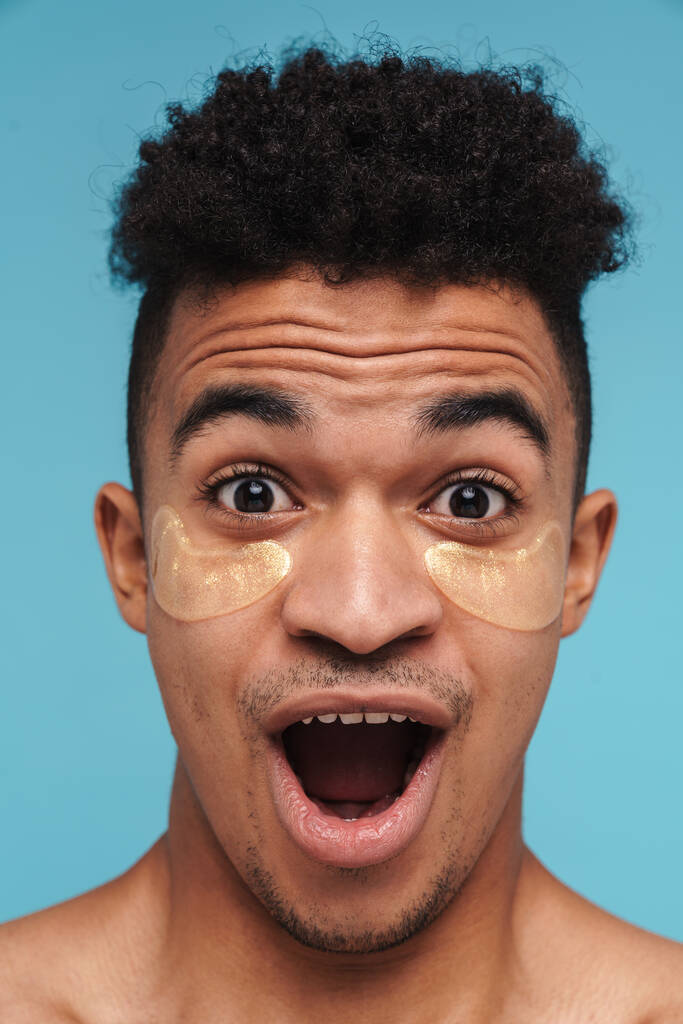 Photo of shocked african american man with under eye patches looking at camera isolated over blue background - Photo, Image