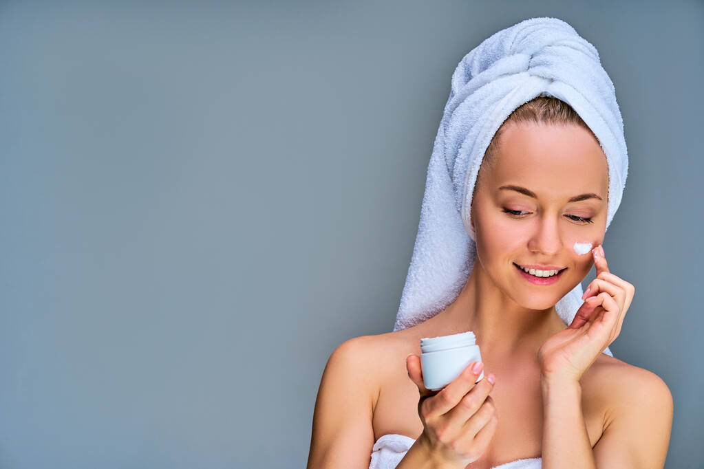 Femme heureuse dans une serviette de bain blanche avec une serviette blanche sur ses cheveux avec pot de crème
 - Photo, image