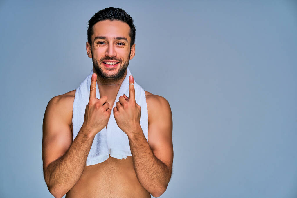 Glücklicher Mann mit weißem Badetuch am Hals, Zahnseide über Zeigefinger gestreckt - Foto, Bild
