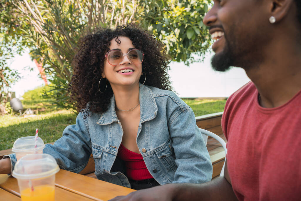 Retrato de dos amigos afro divirtiéndose juntos y disfrutando de un buen rato mientras beben jugo de fruta fresca al aire libre en la cafetería. - Foto, imagen